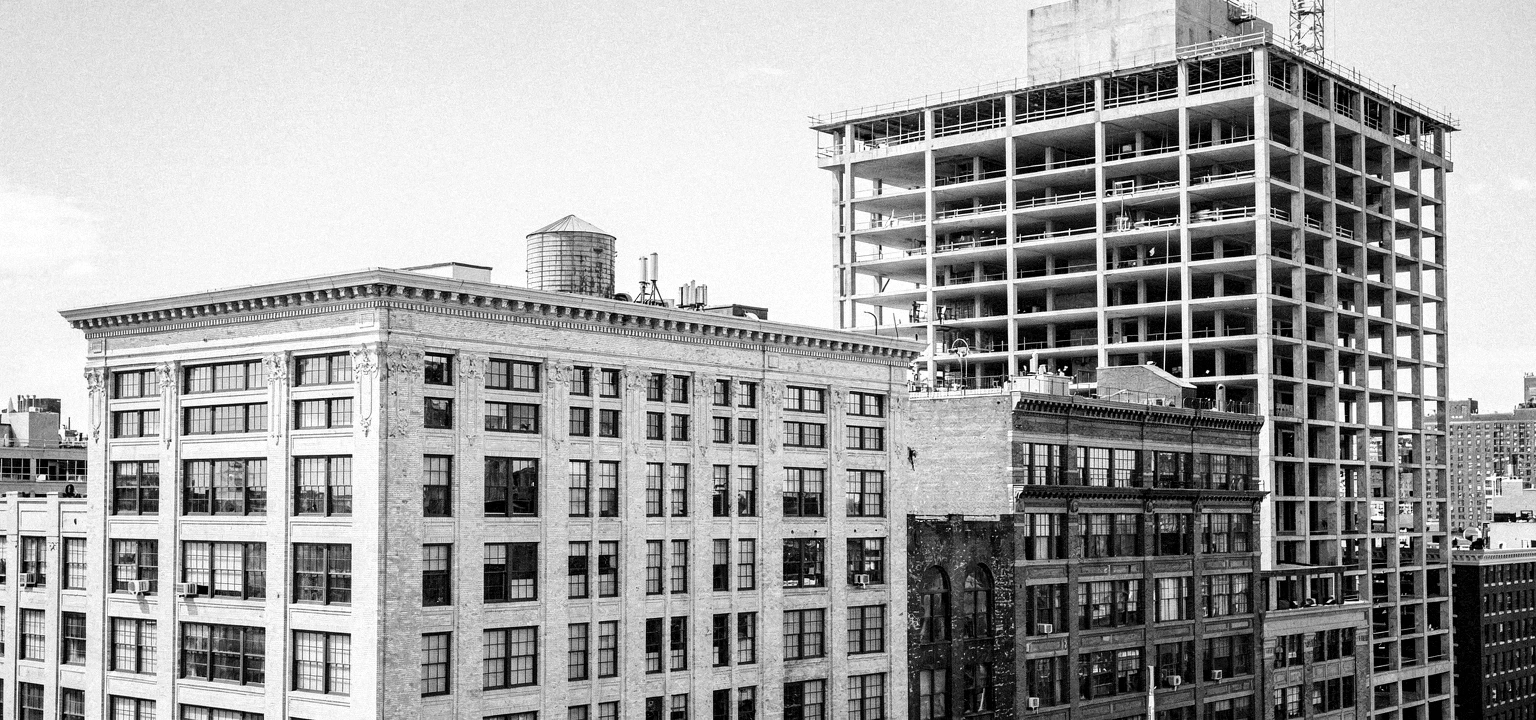 Historic masonry loft buildings beside a concrete building under construction.