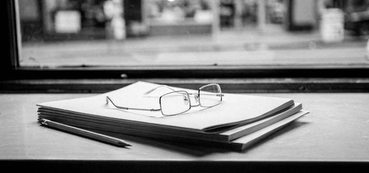 A stack of printed storefront reports with reading glasses and a pencil by a window — the tools of a retail property researcher.