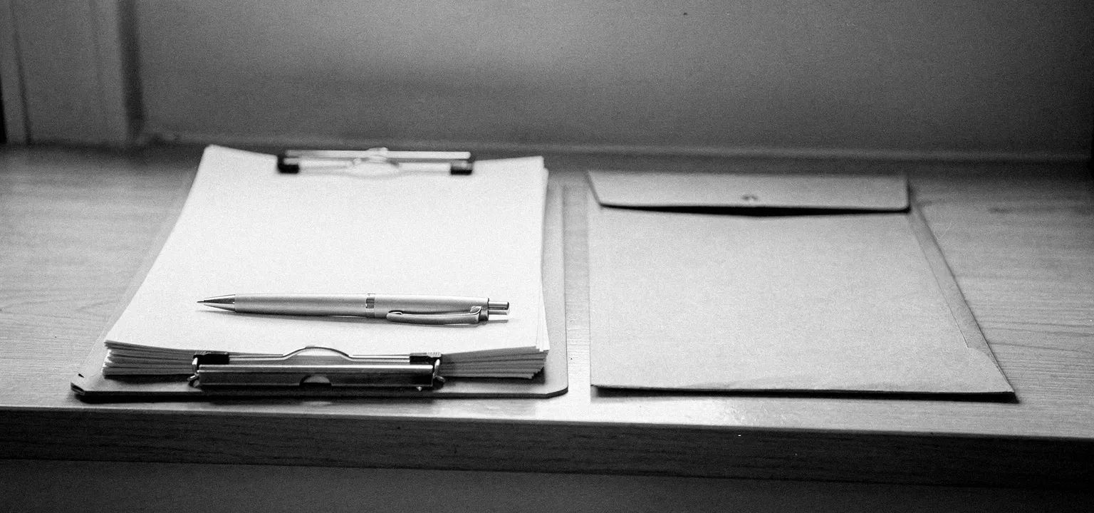 A clipboard holding blank application forms with a pen and a manila folder, the paperwork of gathering a tenant's application.