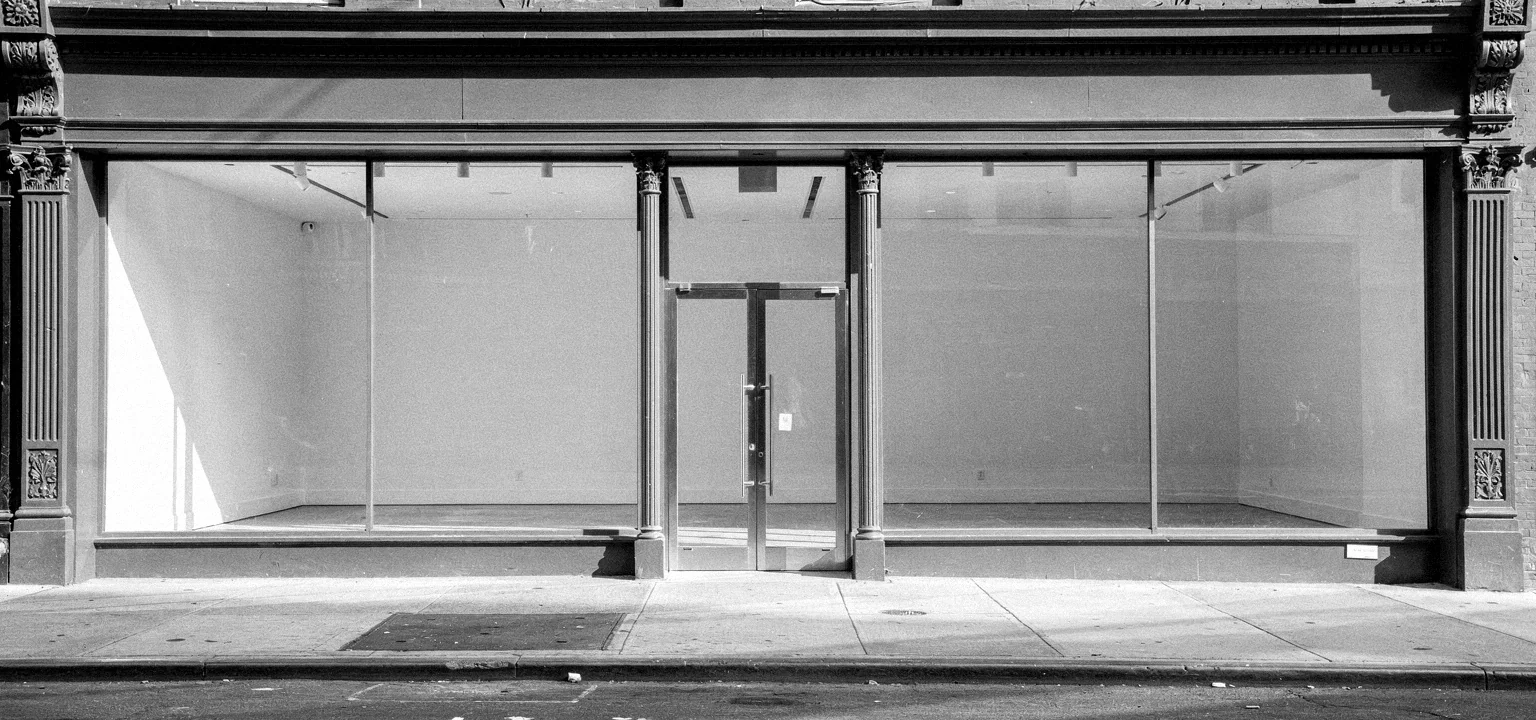 Empty SoHo storefront with cast-iron facade, glass windows, sidewalk and curb.