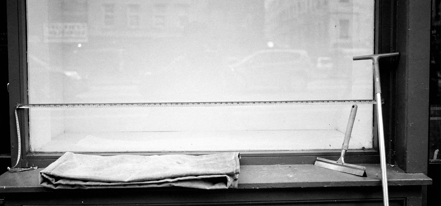 A measuring tape and drop cloth at a blank storefront window, the quiet before moment of preparing a space for a new lease.